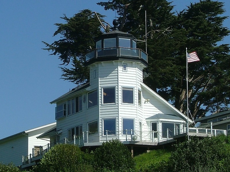 a white house with a flag on top with Pelican Bay Light in the background